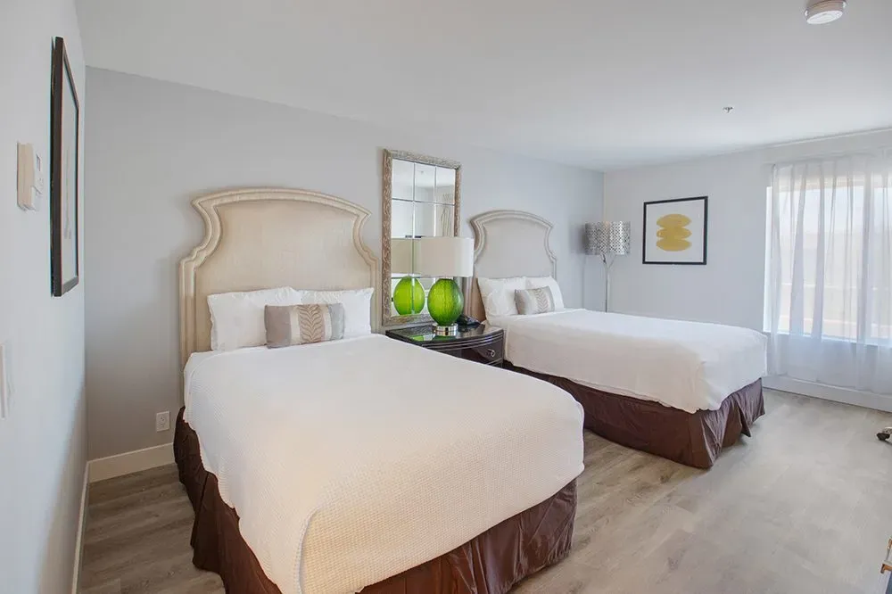 A renovated Elkotel guest room with two beds, tall upholstered headboards and green lamps